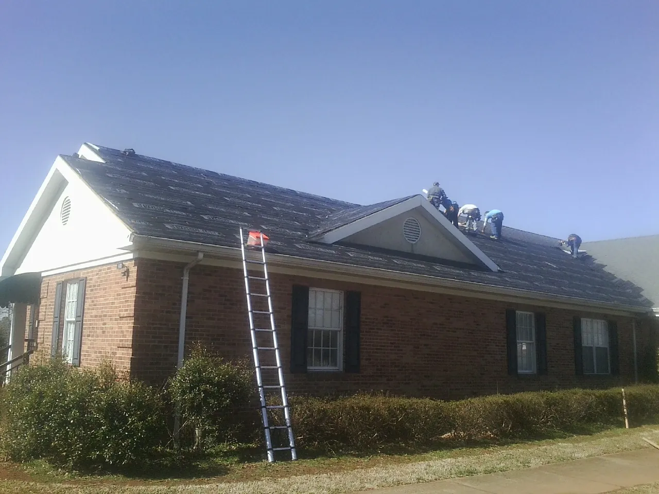 Crew tearing shingles off a brick ranch roof with a ladder set — Emergency Roof Repair work by our crew in Maywood