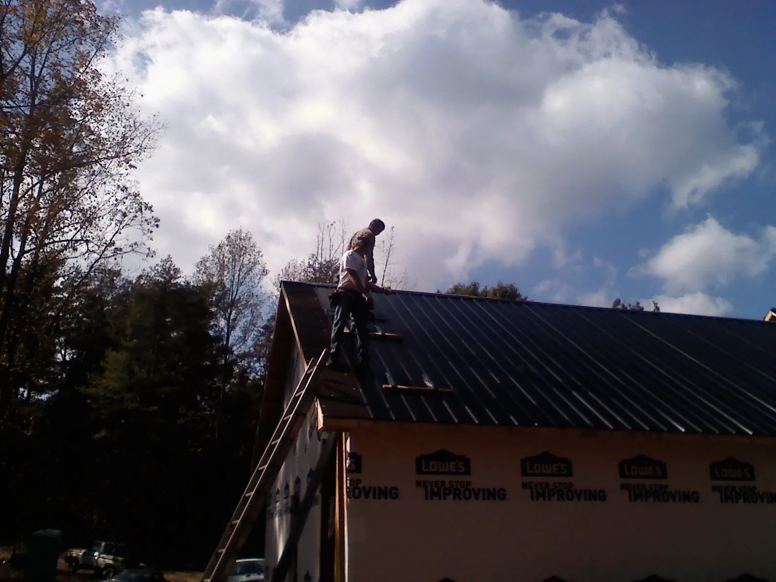 Roofer fastening dark metal panels high against a cloudy sky, from a Roof Inspection job in Maywood